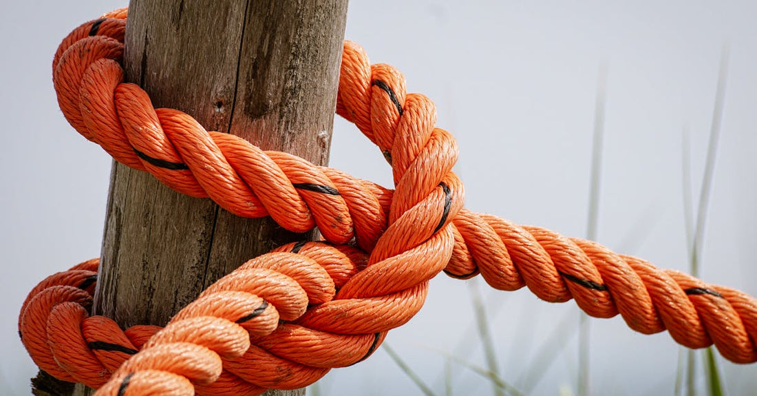 Detailed view of a bright orange rope tied securely around a weathered wooden post in an outdoor setting.