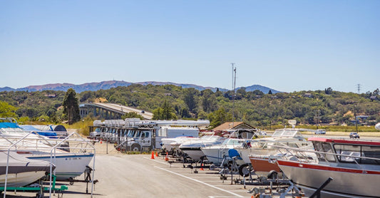A scenic marina with boats and RVs parked under a clear blue sky, surrounded by greenery.