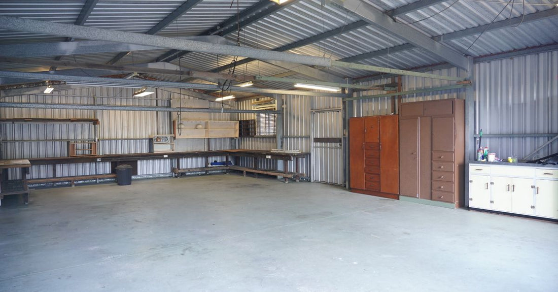 Empty industrial garage with steel walls and ceiling, featuring storage cabinets and workbenches.