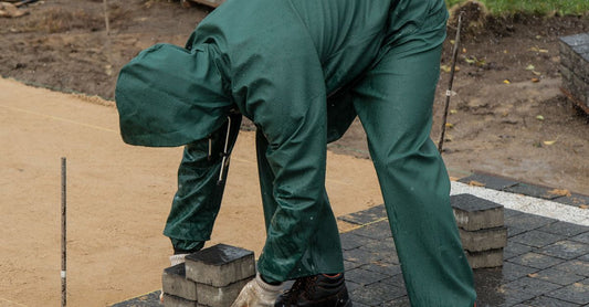 Man laying pavers in an outdoor setting, wearing green rain gear. Concept of construction work.