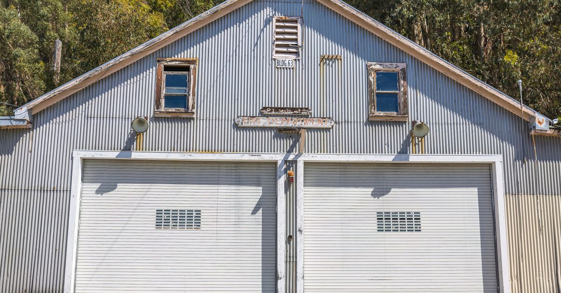 A sunlit vintage metal garage with double doors and rustic charm amidst trees.