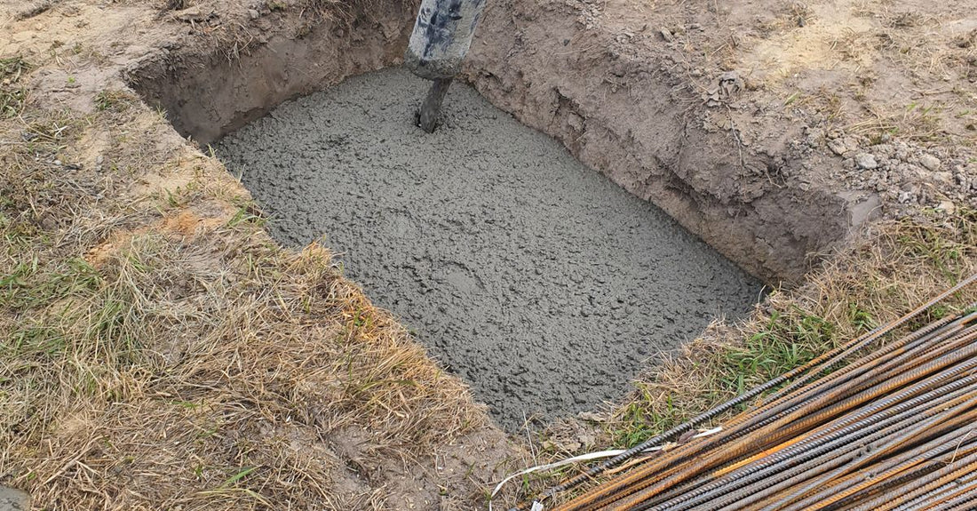 Concrete being poured into a foundation pit at a construction site in Poland, showing rebar and worker boots.
