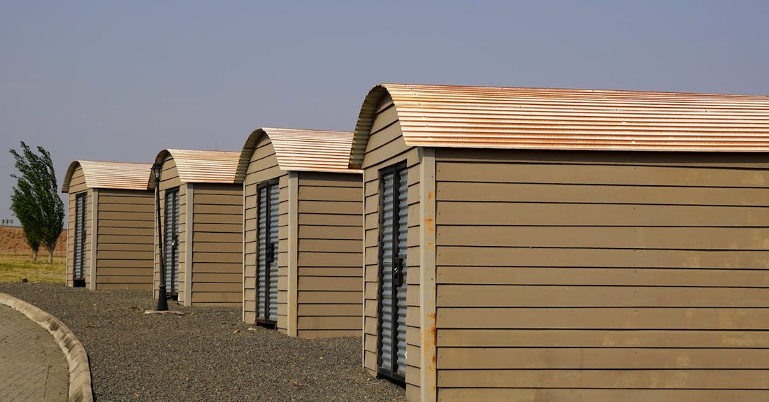Four identical modern storage sheds aligned on a gravel surface with clear skies.