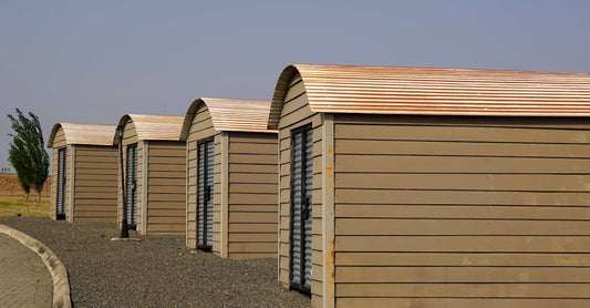 Four identical modern storage sheds aligned on a gravel surface with clear skies.