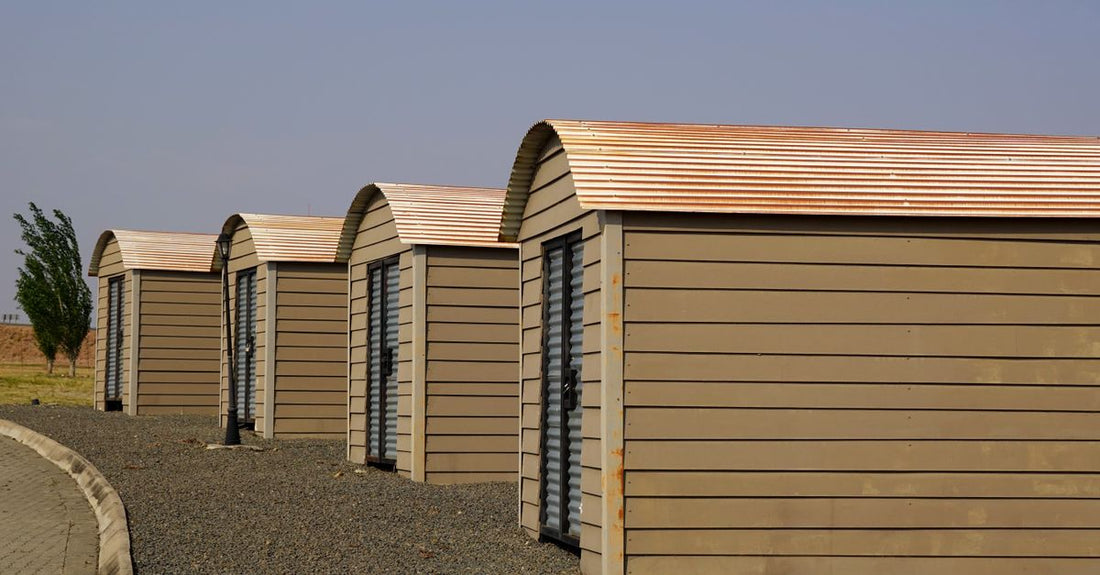 Four identical modern storage sheds aligned on a gravel surface with clear skies.