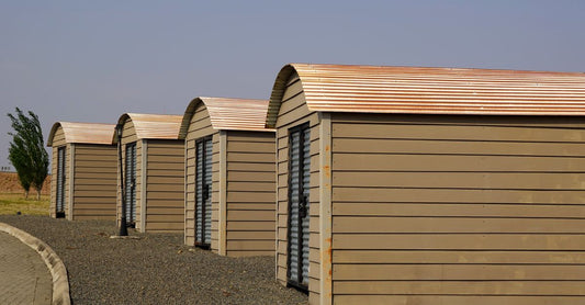 Four identical modern storage sheds aligned on a gravel surface with clear skies.
