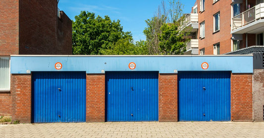 Three blue garage doors in a brick building on a sunny day.