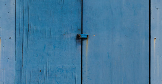 Rustic blue wooden garage door with metal hinges on barn exterior.