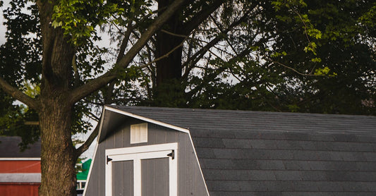 A quaint gray garden shed nestled under lush trees in a serene backyard.