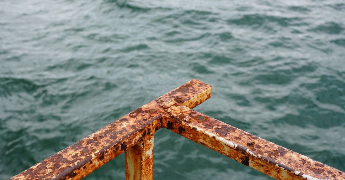 Close-up of a rusted metal railing with ocean waves in the background, suggesting decay and nature's force.