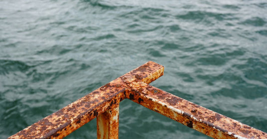 Close-up of a rusted metal railing with ocean waves in the background, suggesting decay and nature's force.
