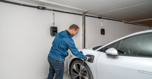 A man connects an electric car to a charging station in a modern indoor garage setting.