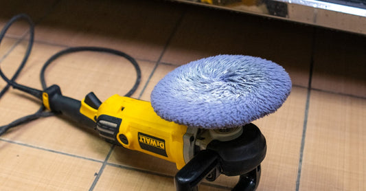 A yellow electric car polisher resting on a tiled garage floor, next to a vehicle.