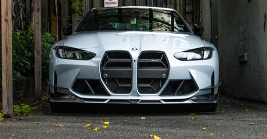 Front view of a sleek silver car parked under a wooden carport in an outdoor setting.