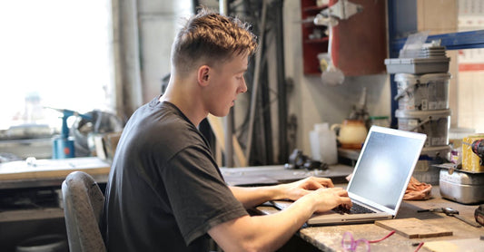 Focused man working remotely from a garage workshop using a laptop.