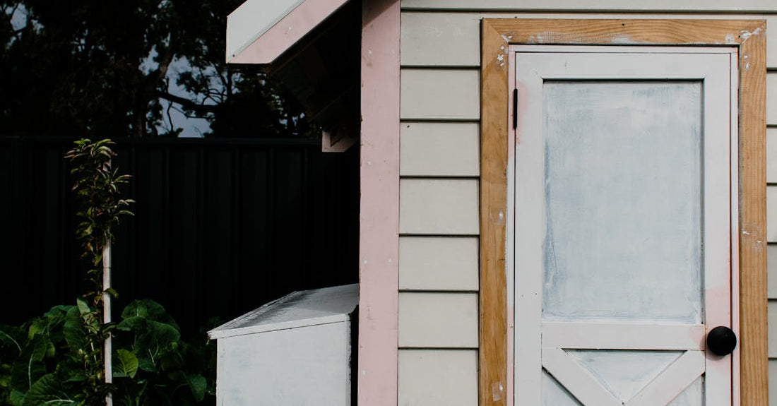 A small wooden shed surrounded by greenery under an overcast sky, showcasing rustic charm.