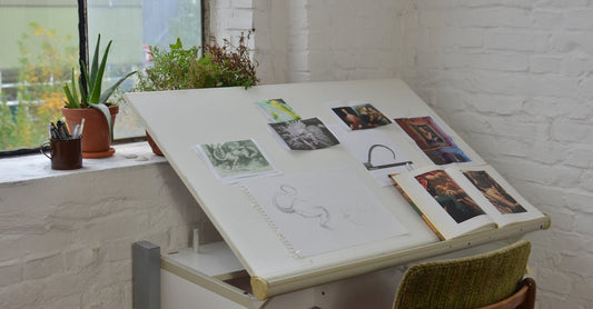 Cozy artist's workspace featuring sketches, art supplies, and plants by a window.