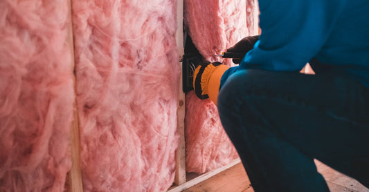 Focused worker installing pink fiberglass insulation in a building interior.