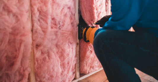 Crop unrecognizable worker in gloves sitting on haunches and insulating with pink stone wool