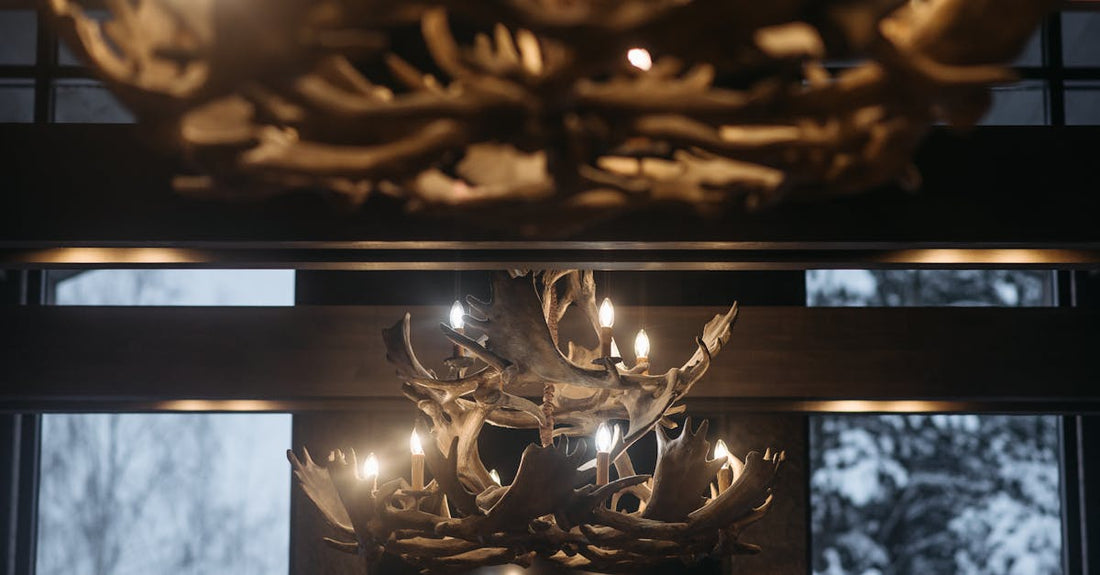 Warm lighting from antler chandeliers in a cozy winter cabin with snow visible outside.