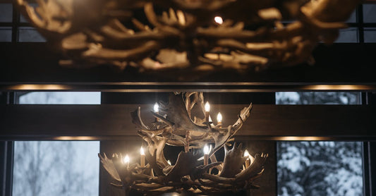 Warm lighting from antler chandeliers in a cozy winter cabin with snow visible outside.