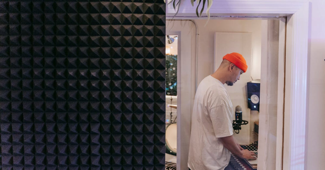Side view of a man in a music studio with soundproof material, focused on a laptop.