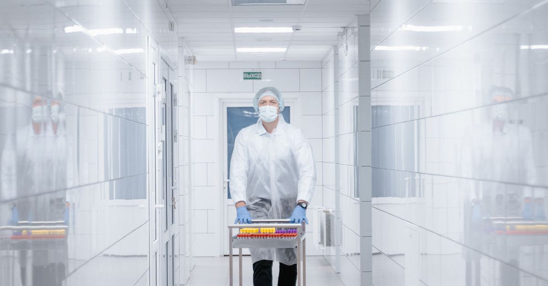 Scientist in protective clothing walking with cart in a sterile laboratory corridor.